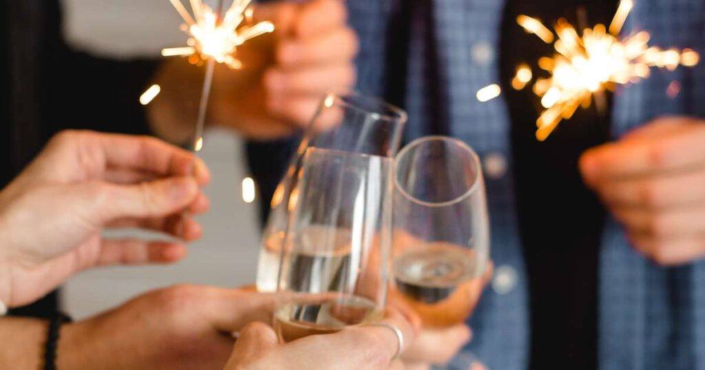 group of hands clinking champagne glasses and holding sparklers
