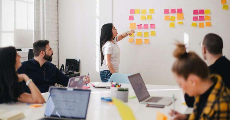 team member presenting at whiteboard with sticky notes to a group in the conference room