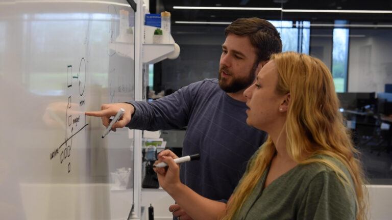 Two software engineers working together problem-solving at a white board.