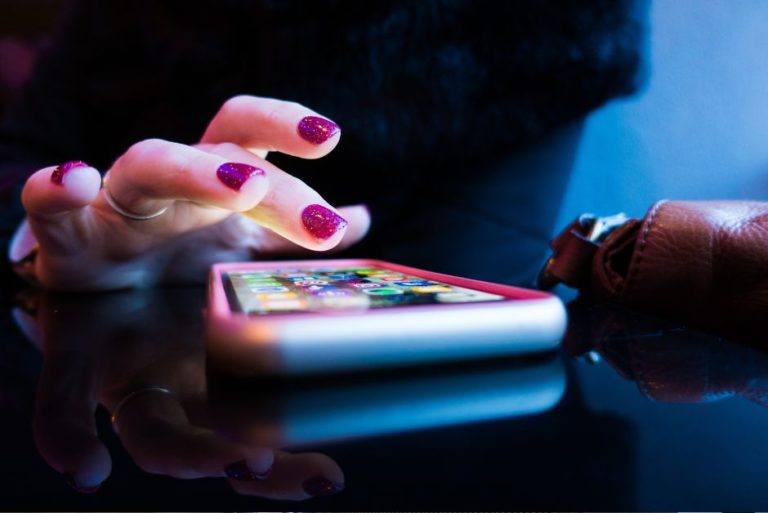 person with painted nails tapping smartphone screen on the table