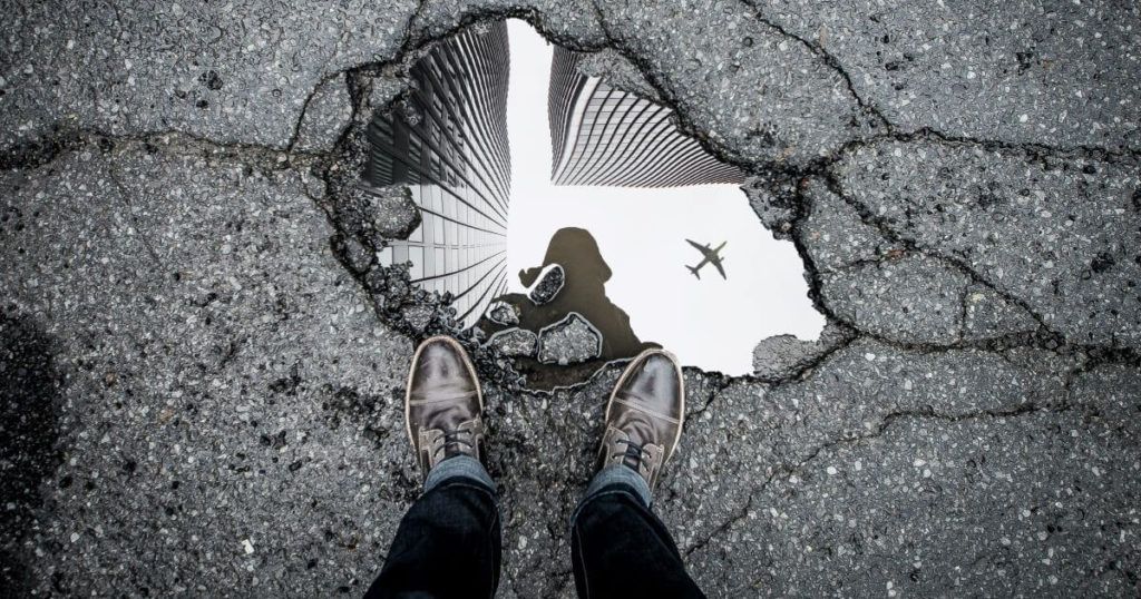 Person looking at their reflection in a water-filled pothole. Photo by Marc-Olivier Jodoin on Unsplash