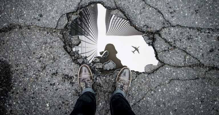 Person looking at their reflection in a water-filled pothole. Photo by Marc-Olivier Jodoin on Unsplash