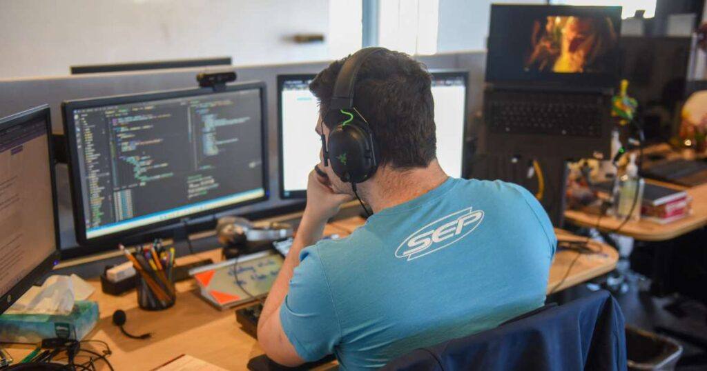 Software developer in SEP t-shirt examines code on computer screen