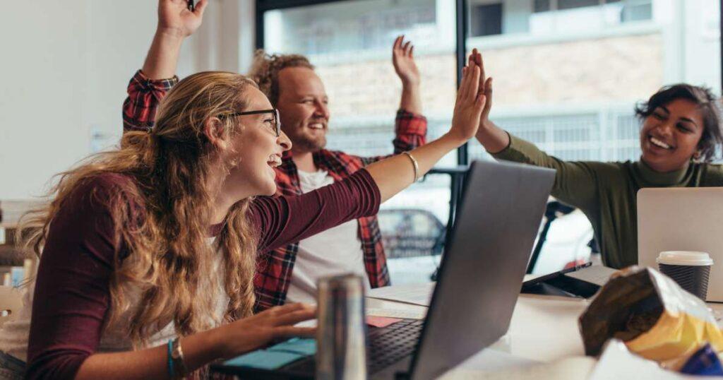 team high fiving and celebrating over a laptop