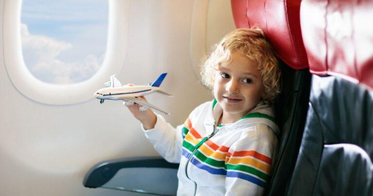 happy little girl holding toy plan in airplane window seat