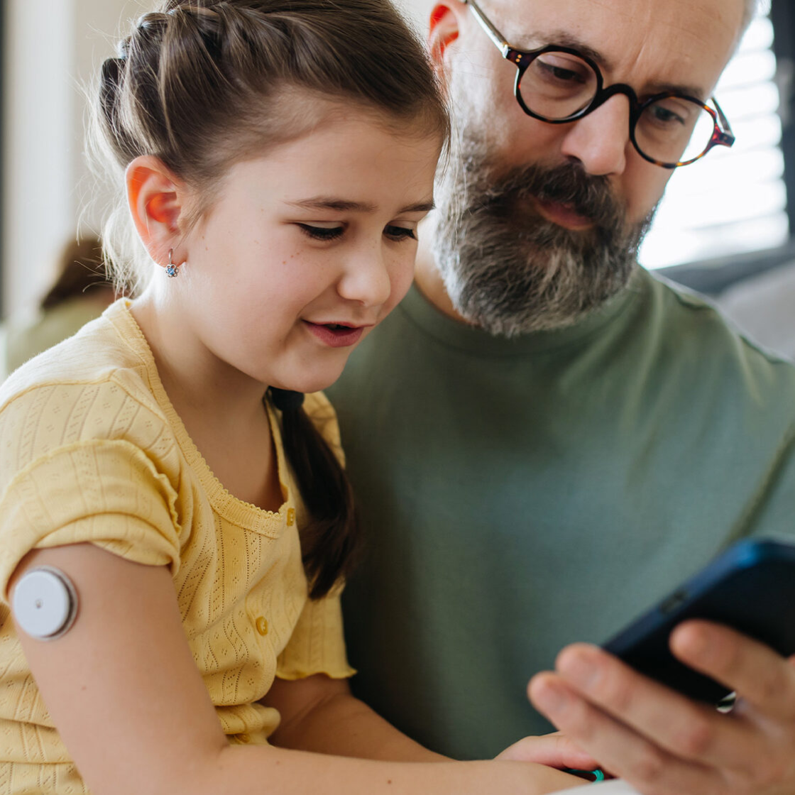 dad and daughter checking phone while daughter wears a diabetes glucose monitor