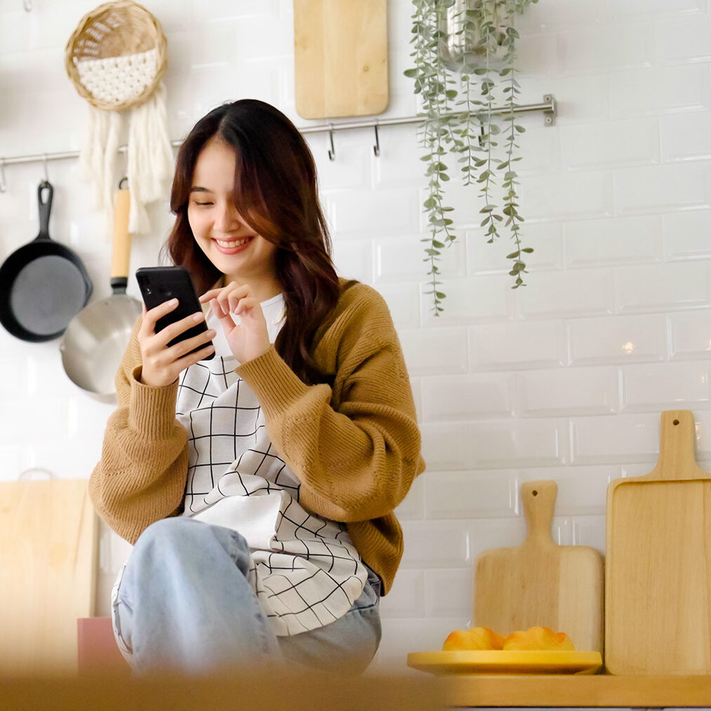 girl smiling tapping mobile phone while sitting on kitchen counter