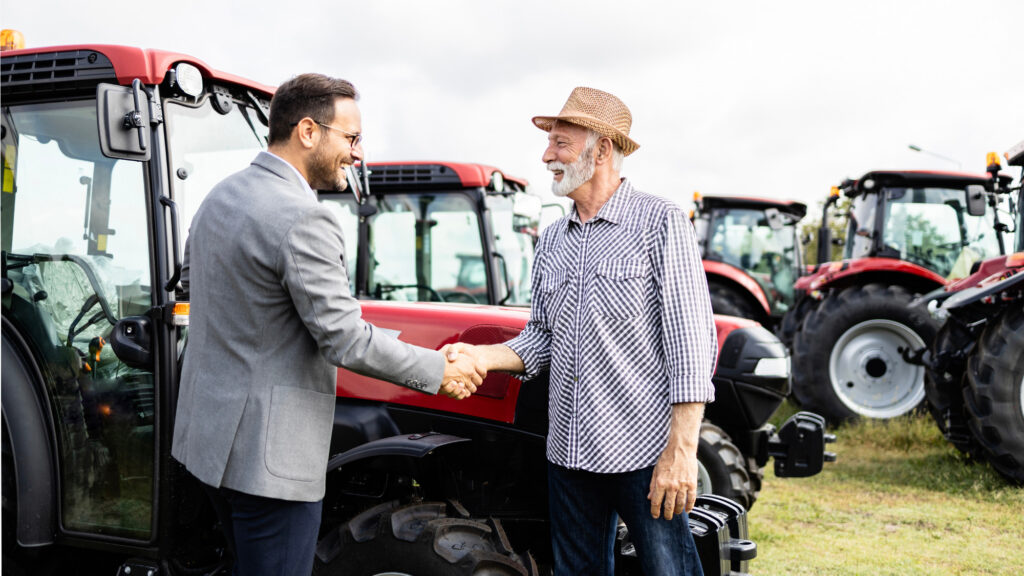 Two men shake hands in front of some tractors
